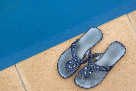 A pair of fashionable ladies slip-on shoes, next to the pool.