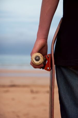 A skateboarder holding his board. Beach background with plenty of copy-space.の写真素材