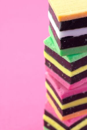A stack of colorful liquorice allsorts on a pink background.のeditorial素材