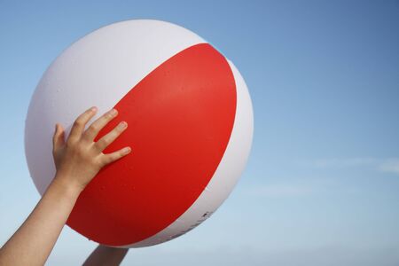 A colorful beach ball held up against the blue summer sky.の写真素材
