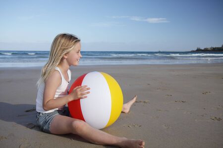 A young girl plays with a beach ball on the sand.の写真素材