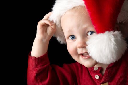 A gorgeous young boy peeking out from behind a santa hat.の写真素材