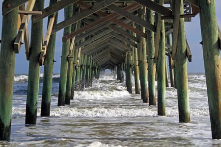 Waves crash through the pilings beneath a pier