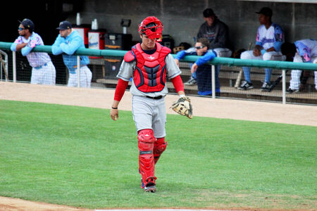 A professional baseball catcher walks off of the field at the end of an inning 