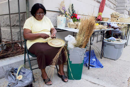 A Sweetgrass basket maker shows off practices her art on Meeting street in Charleston, South Carolina, USA. A skill passed down from the African slaves, sweetgrass basket making is a dying art.Unique to the South Carolina Lowcountry,they are created from のeditorial素材