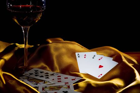 poker ace and a glass of wine on a golden silk. low key shot with focus on the 4 の写真素材