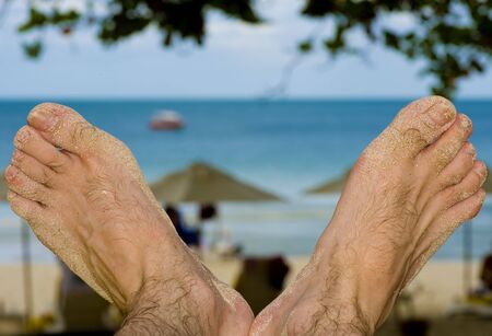 the view of a man watching the beach through his feetの写真素材
