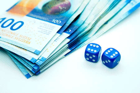 Two blue dices next to Swiss franc bills with a white background