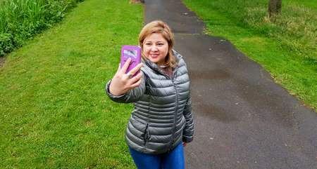 Latin woman in a gray anorak making a selfie with the mobile phone in the middle of a landscaped...