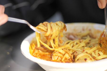 Hands of man eating Thai noodle curry soup