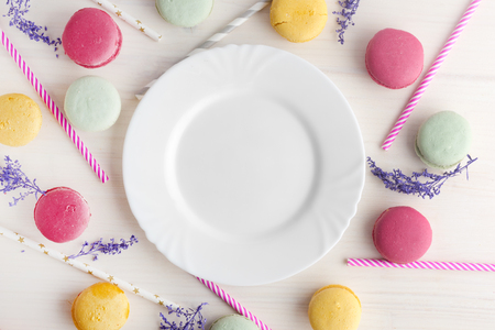 An empty, white plate, with a delicious dessert around, macaroons and tubes for a cocktail. Place for text. Festive layout, template.の写真素材