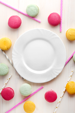 An empty, white plate, with a delicious dessert around, macaroons and tubes for a cocktail. Place for text. Festive layout, template.の写真素材
