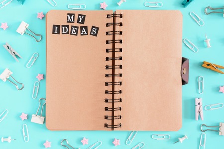 My Ideas. Notepad with brown sheets and an inscription on the open page. Chaos of stationery. Clips, clothespins and small sprockets scattered .の写真素材