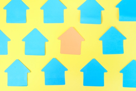 Turquoise stickers in the form of a house on a yellow background. In the center, the empty sticker is pale orange. Beautiful layout, mock up. Photo from the top.の写真素材