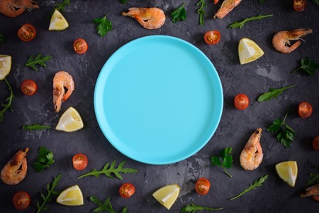 An empty blue plate lies in the center of a dark textured background. Around are scattered lemon,...