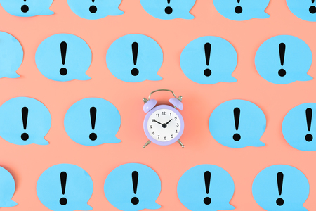 Blue stickers with exclamation marks on a pink background. In the center is a small pink alarm clock. Concept, attention time. Bright photo from the top.の写真素材