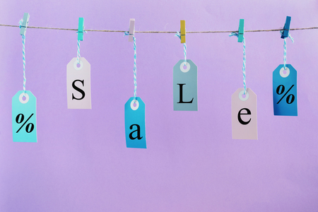 Labels hang on the rope with attached clothespins. They inscription SALE. Photo on a lilac background.の写真素材