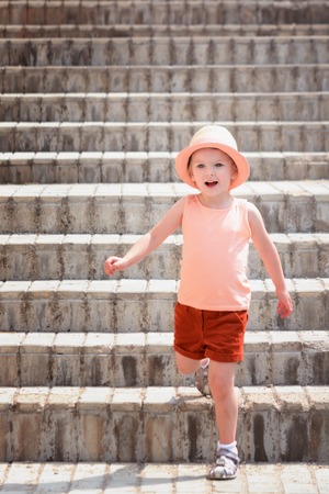 The little joyful girl went down the stairs. A child wearing a stylish hat and red shorts.