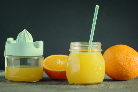 Freshly squeezed orange juice in a jar with a straw. Nearby is a juicer and oranges.の写真素材