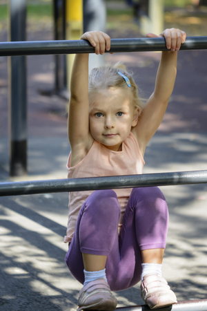 The child is doing exercise on the sports field. A little girl with blond hair.