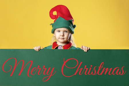 Little girl in an elf costume. On a green background there is an inscription of Merry Christmas.の写真素材