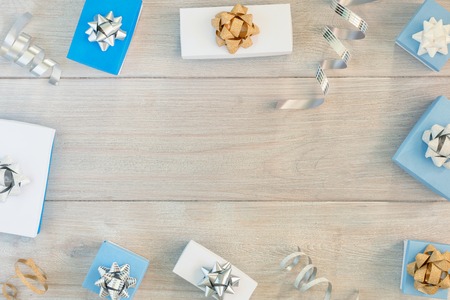 Christmas card with place for text, copy space. Small gift boxes and ribbons lie in a circle on a light wooden background.の写真素材
