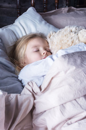 The little girl is sleeping in an embrace with a toy bear. Cute baby in the bed.の写真素材