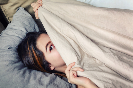 Cheerful girl with dark hair, hides her face under a blanket.の写真素材