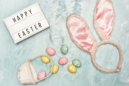 On a blue  are the ears of a rabbit costume. Near the basket with painted little eggs.の写真素材