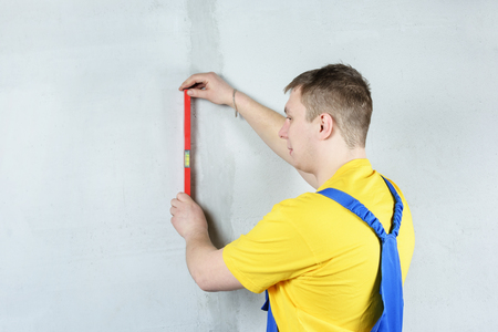 A man in working form checks the flatness of the wall with the help of a building level.