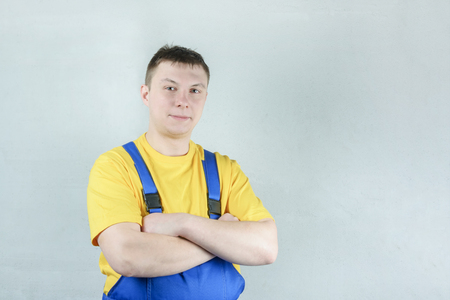A male repairman in a blue jumpsuit and a yellow t-shirt against a gray wall. Near place for text.の写真素材
