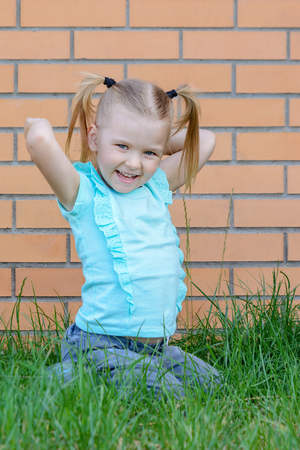 Little girl in blue t-shirt is sitting in the grass.の写真素材