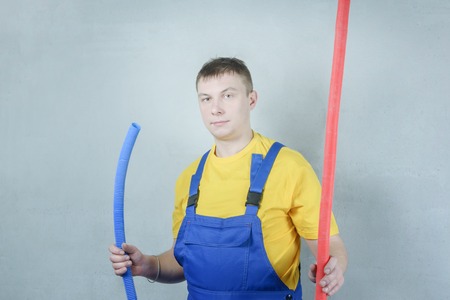 A man in work clothes against a gray wall. A plumber worker is holding a pipe.