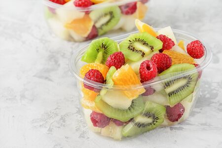 Fresh Sliced Tropical Fruits Berries in Container. Delicious Healthy Snack Ready to Eat Salad in Transparent Cup Closeup Elevated View. Vegetarian Raw Food. Citrus, Kiwi, Raspberries for Lunchの写真素材