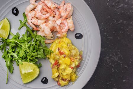 On a gray plate are shrimp, mango chutney sauce and arugula salad. Photo above. Copy space.の写真素材