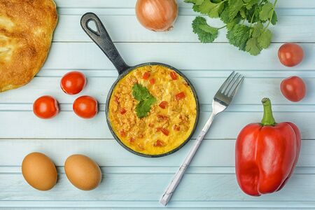 On a blue background, a pan with a Turkish national recipe. Omelet made from eggs, tomato, onion and pepper, Menemen. Flat lay.の写真素材