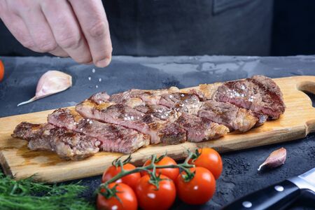 Marbled beef steak. The man is salting the medium-rare meat. Freshly made chuck roll steakの写真素材