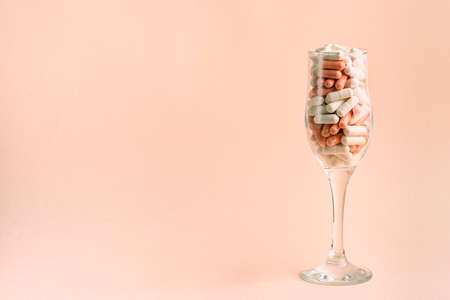 Glass with pink and white capsules. Medicines instead of a party. Copy spaceの写真素材