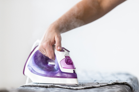 Iron on ironing board on light home interior background. Ironing bed linenの写真素材