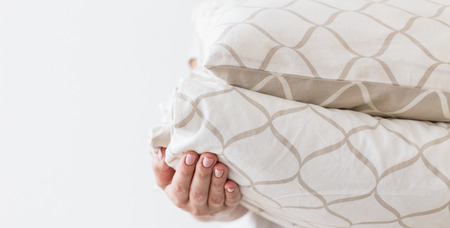 Hands of woman holding modern beige bed linen pile, white wall background in trend, minimalism clean...