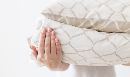 Hands of woman holding modern beige bed linen pile, white wall background in trend, minimalism clean home conceptの写真素材