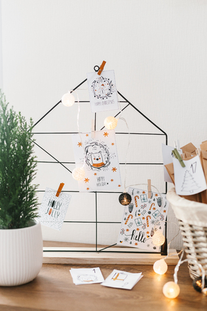 Advent calendar waiting for Christmas. Wire decor note board with christmas cards. Basket with envelopes with numbers and tasks for children standing on cabinetの写真素材