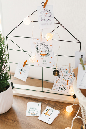 Advent calendar waiting for Christmas. Wire decor note board with christmas cards. Basket with envelopes with numbers and tasks for children standing on cabinetの写真素材