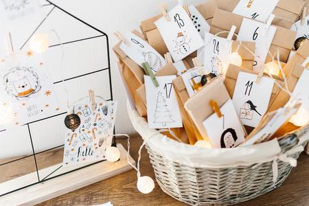 Advent calendar waiting for Christmas. Wire decor note board with christmas cards. Basket with envelopes with numbers and tasks for children standing on cabinetの写真素材