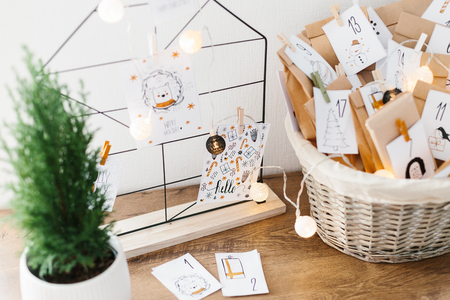 Advent calendar waiting for Christmas. Wire decor note board with christmas cards. Basket with envelopes with numbers and tasks for children standing on cabinetの写真素材
