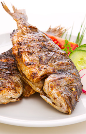 Close-ups of two dorada fish with vegetables  and onion isolated on white. Fried fish.の写真素材