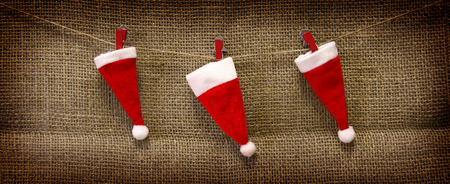 Christmas accessories hanging on  brown cloth  background.Three red  christmas hats isolated on brown  background.の写真素材