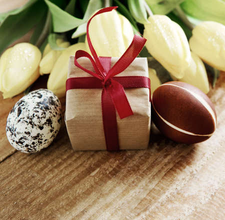 Colorful easter eggs with yellow tulip flowers and gift box  isolated on wood  background.Easter card.の写真素材