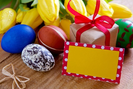 Colorful easter eggs with yellow tulip flowers and gift box  isolated on wood  background.Easter...