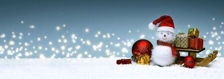 Christmas snowman with gifts on the sledge and snowfall.